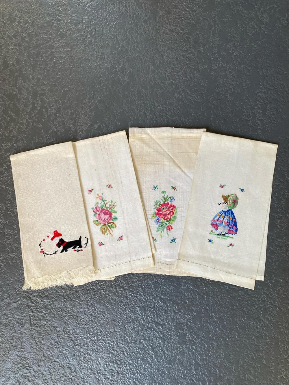 The image shows a set of four vintage hand-embroidered and cross-stitched